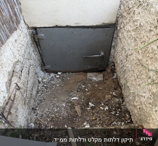 דלת מתכת ישנה בקיר חיצוני עם אדמה מסביב